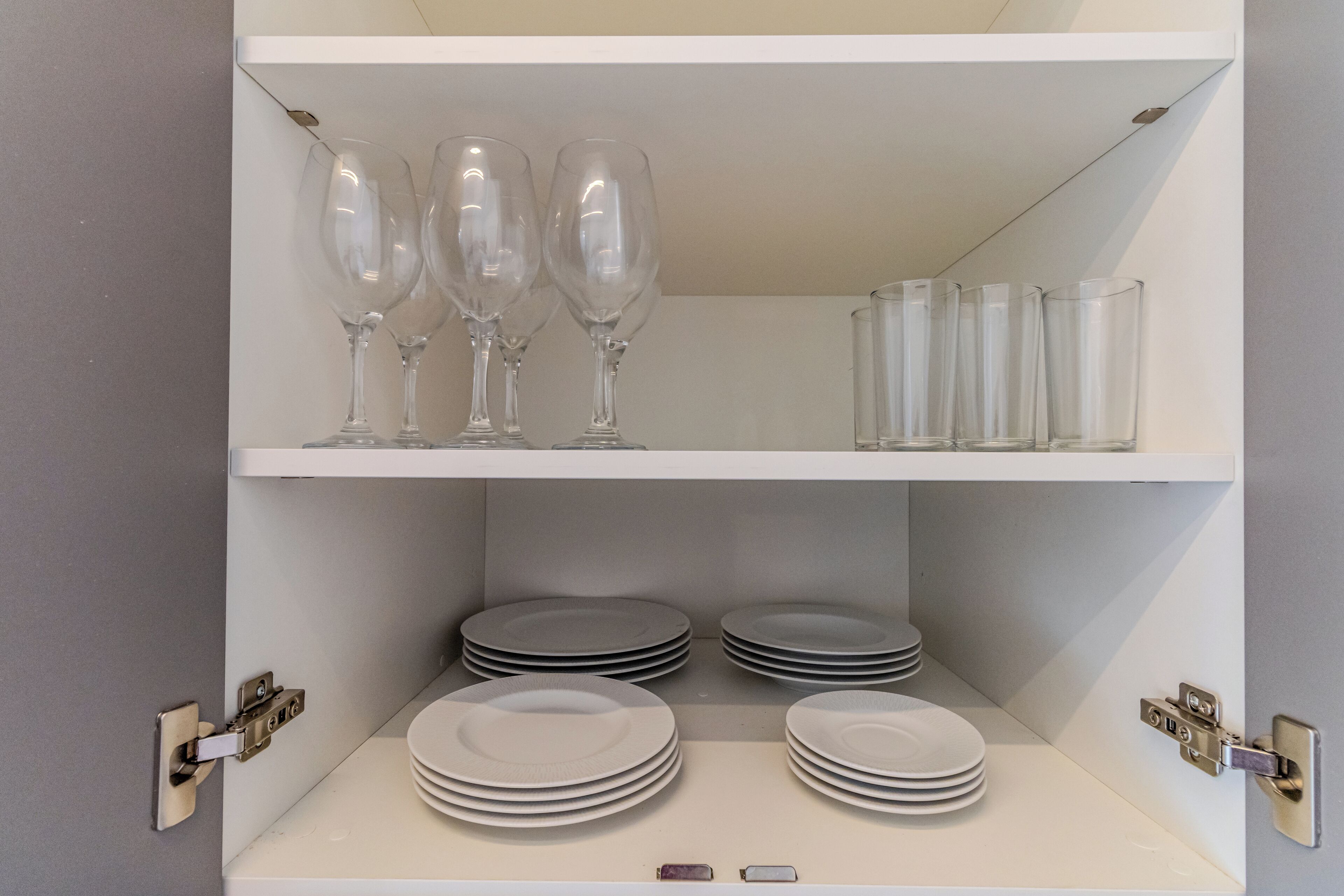 Een witte plankenwand met wijnglazen en borden.