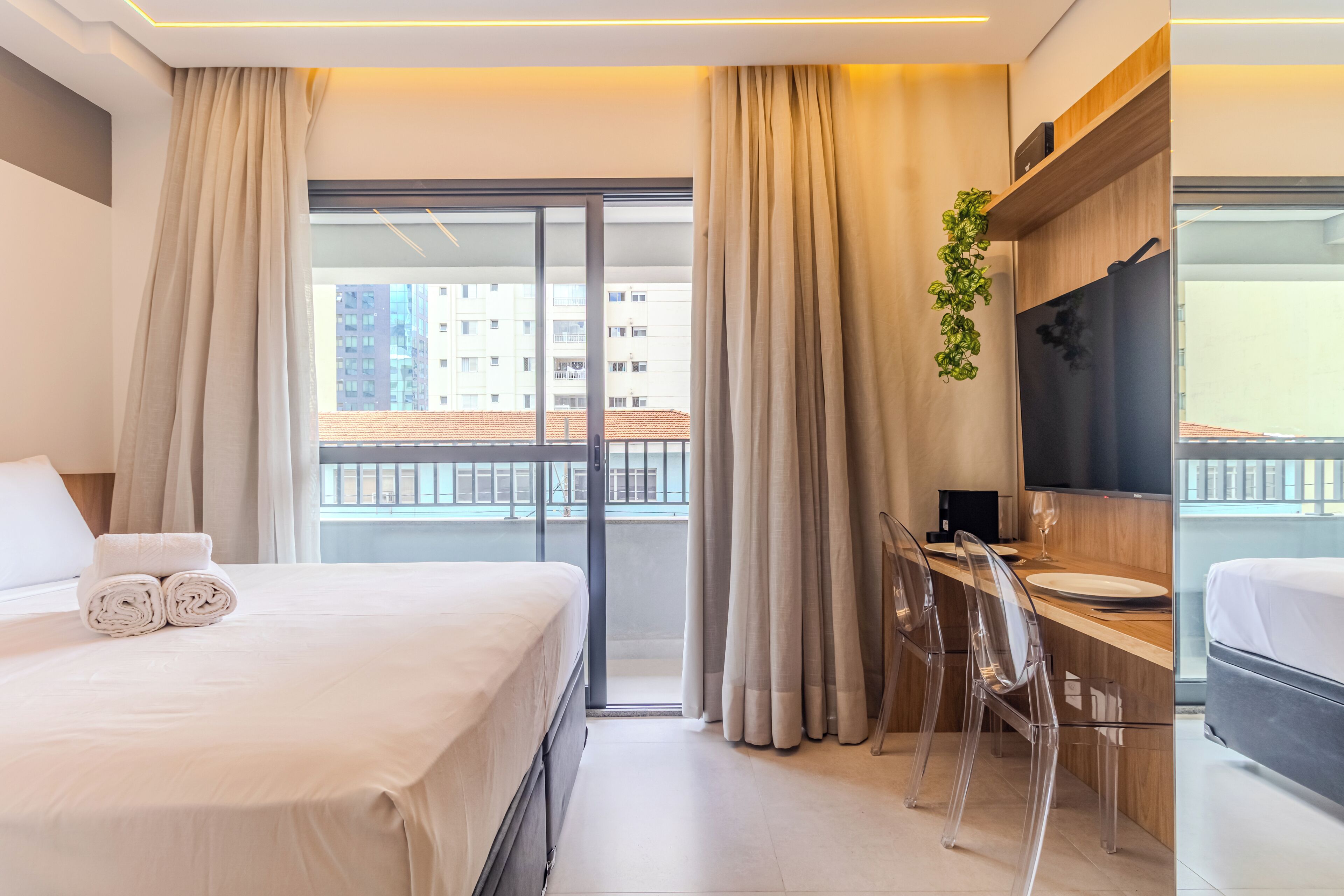 Una moderna camera d'hotel con un letto grande, una scrivania con sedia, una TV a schermo piatto e un balcone con tende.