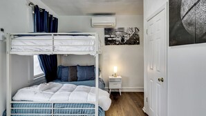A bunk bed room with a bedside table, a wall-mounted air conditioner, and a door with a handle. - Walk to Public Transit! Pet-friendly Lodi Apt (Lodi)