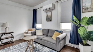 A modern living room with a grey sofa, a round coffee table, and a large potted plant. - Walk to Public Transit! Pet-friendly Lodi Apt (Lodi)