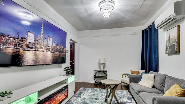 A modern living room with a flat-screen TV, a grey sofa, a patterned rug, and a cityscape painting. - Walk to Public Transit! Pet-friendly Lodi Apt (Lodi)