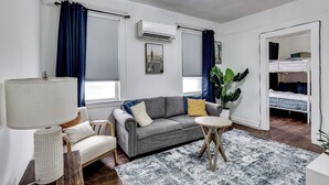 A modern living room with a grey sofa, a round wooden table, a white lamp, and a large potted plant. - Walk to Public Transit! Pet-friendly Lodi Apt (Lodi)