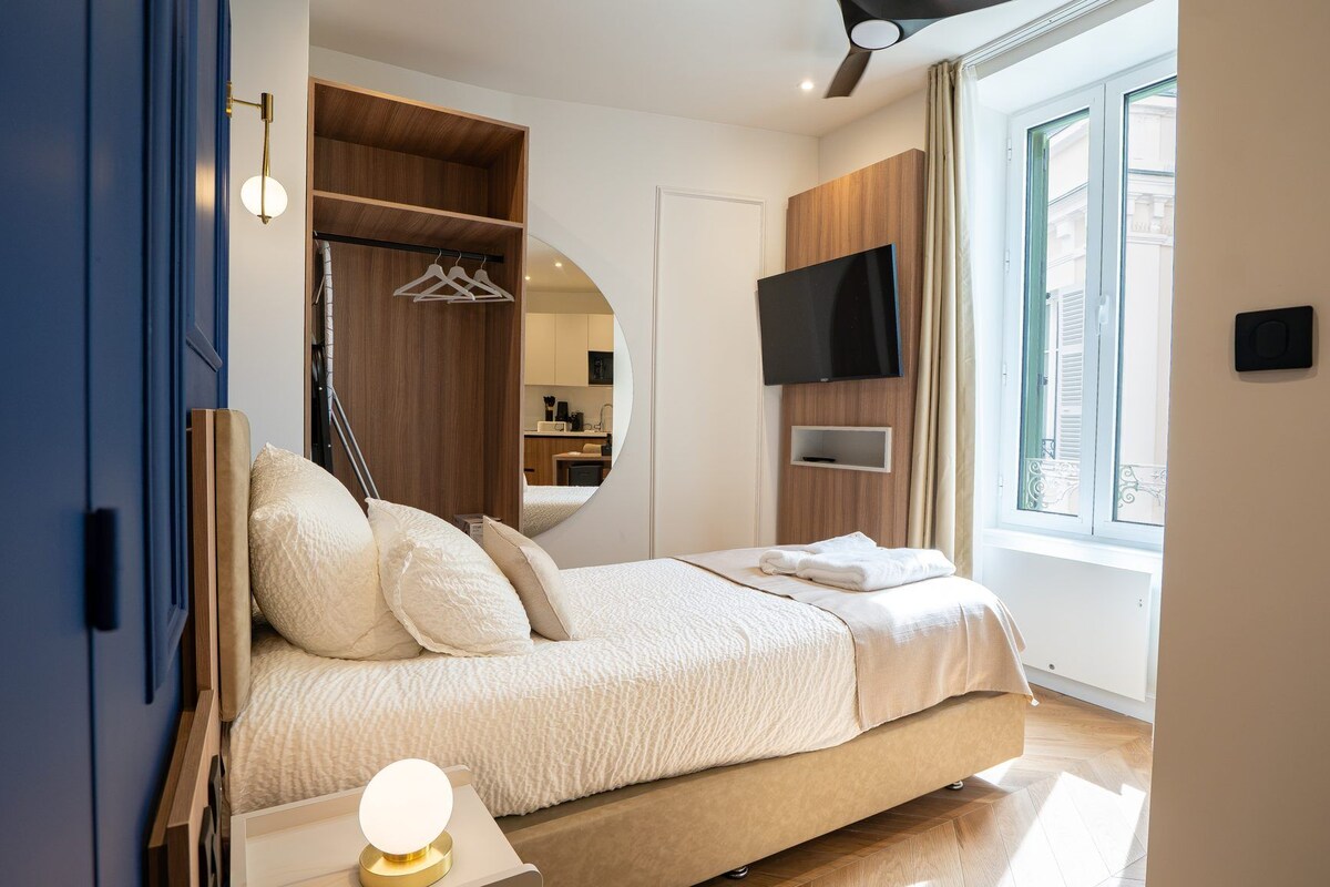 A bedroom with a bed, a TV, a wardrobe, and a window.