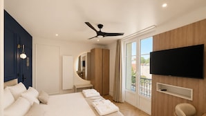 Une chambre d’hôtel moderne dotée d’un grand lit, d’un ventilateur de plafond, d’un téléviseur fixé au mur et d’un balcon avec vue.