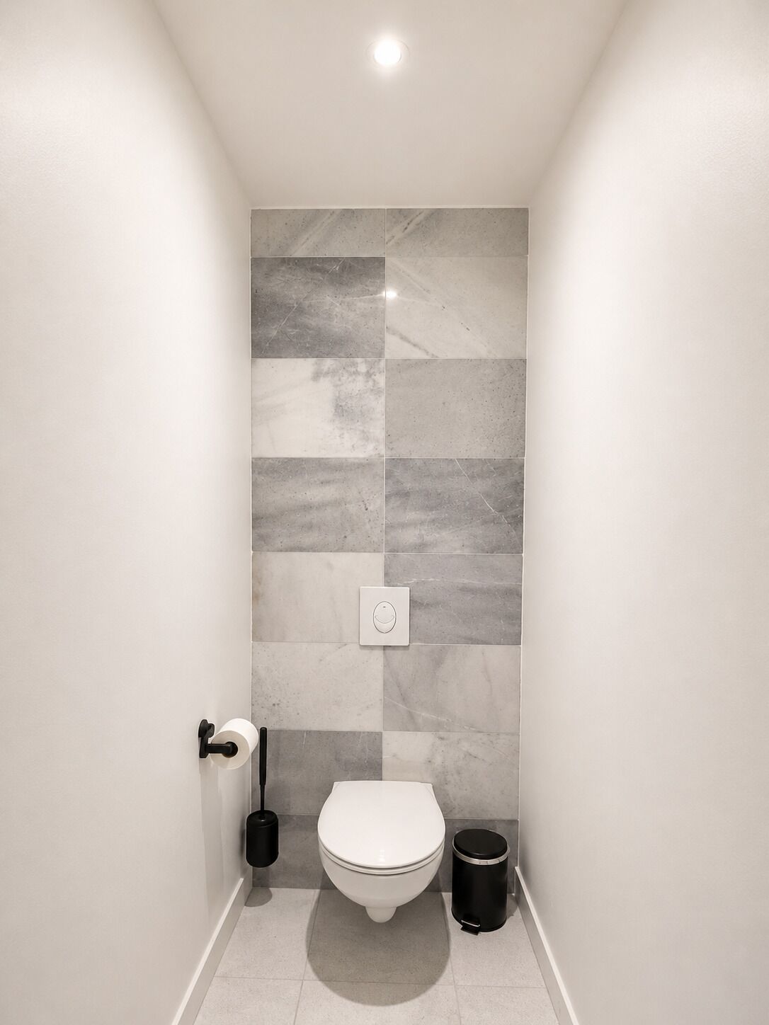 A small, modern bathroom with a toilet, a trash can, and a toilet paper holder.