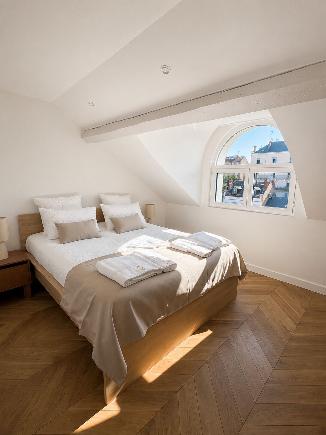 A bedroom with a large bed, a skylight, and a view of buildings.