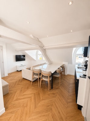 A modern interior with a dining area, kitchen, and a TV mounted on the wall. - The Originals Residence, Les Sources Callou, Vichy (Vichy)