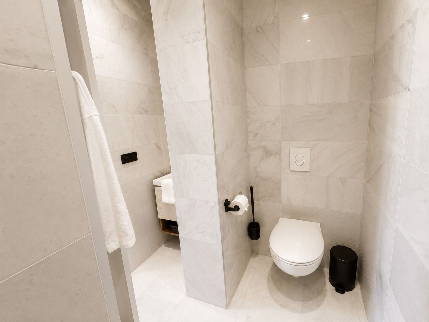 A modern bathroom with a toilet, bidet, and a trash bin.