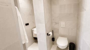 A modern bathroom with a toilet, bidet, and a trash bin.
