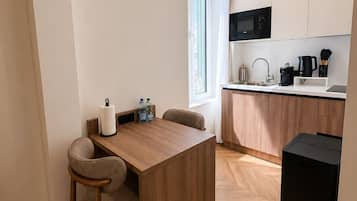 Una cucina compatta con un tavolo di legno, una sedia, un cestino nero e una finestra con tende.