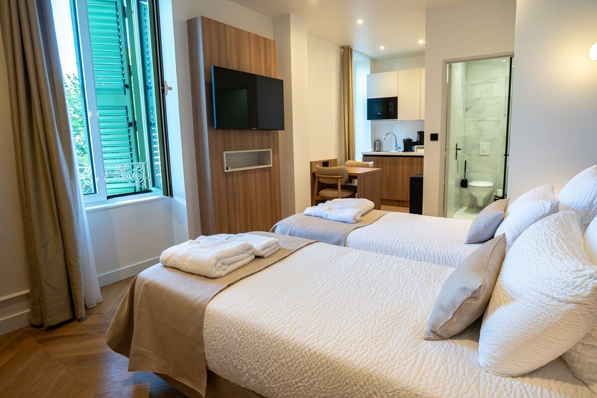 Une chambre d’hôtel avec deux lits, une télévision, un bureau et une salle de bain visible à travers une porte ouverte.