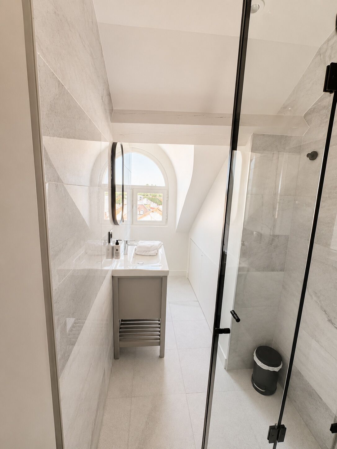 Un bagno moderno con cabina doccia in vetro, un mobile lavabo con specchio e vista dalla finestra.