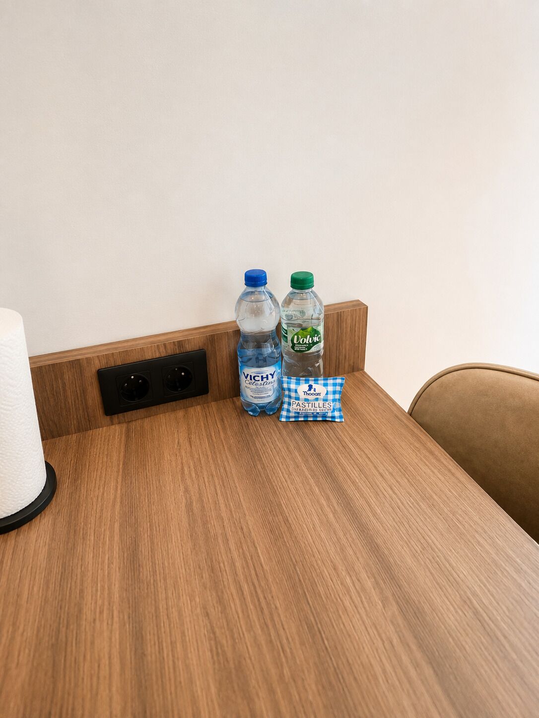 A wooden table with two water bottles, a tissue roll, and a packet of pastilles.