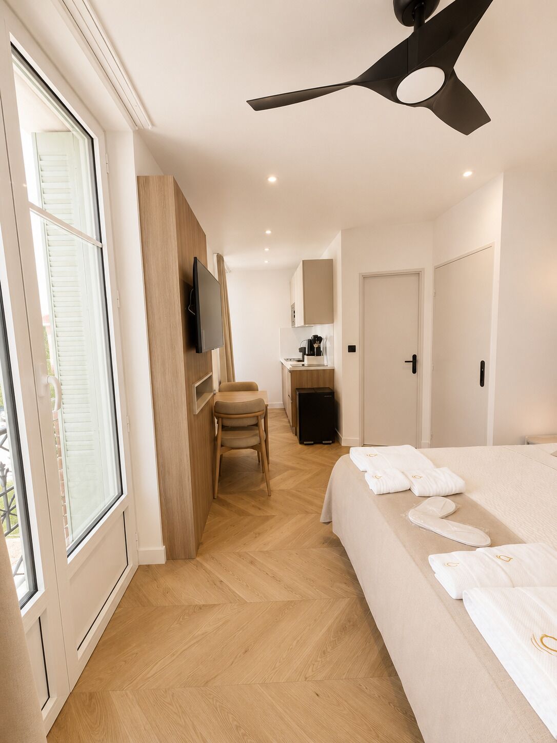 A hotel room with a bed, a desk, a chair, a television, and a ceiling fan.