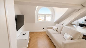 Un dormitorio tipo loft moderno con suelo de madera en espiga, un sofá blanco, un televisor montado en la pared y un tragaluz.