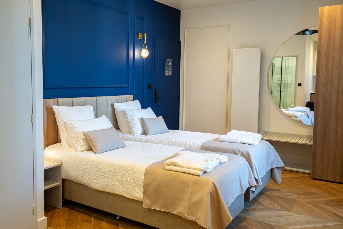 A hotel room with two beds, a mirror, and a wooden floor.