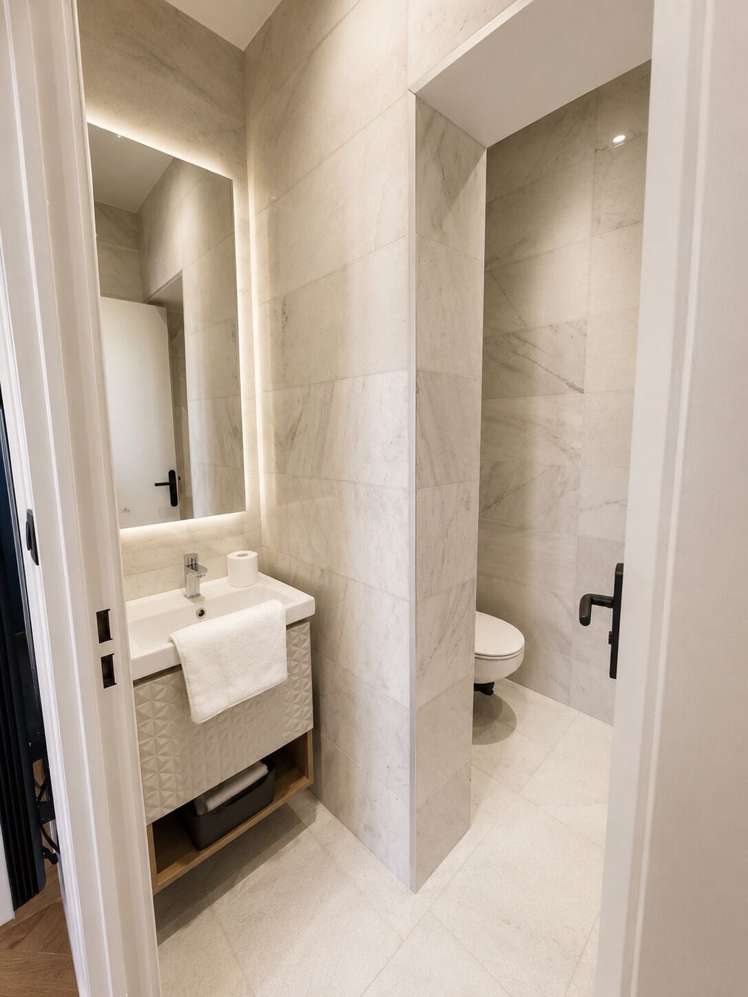 A modern bathroom with a marble wall, a sink, a toilet, and a mirror.