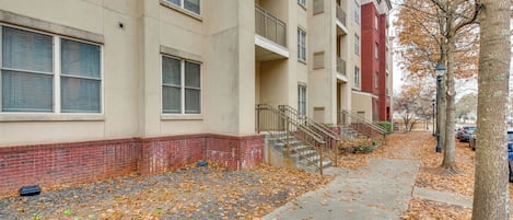 A multi-story residential building with a brick base and beige upper floors, featuring balconies and a visible staircase.