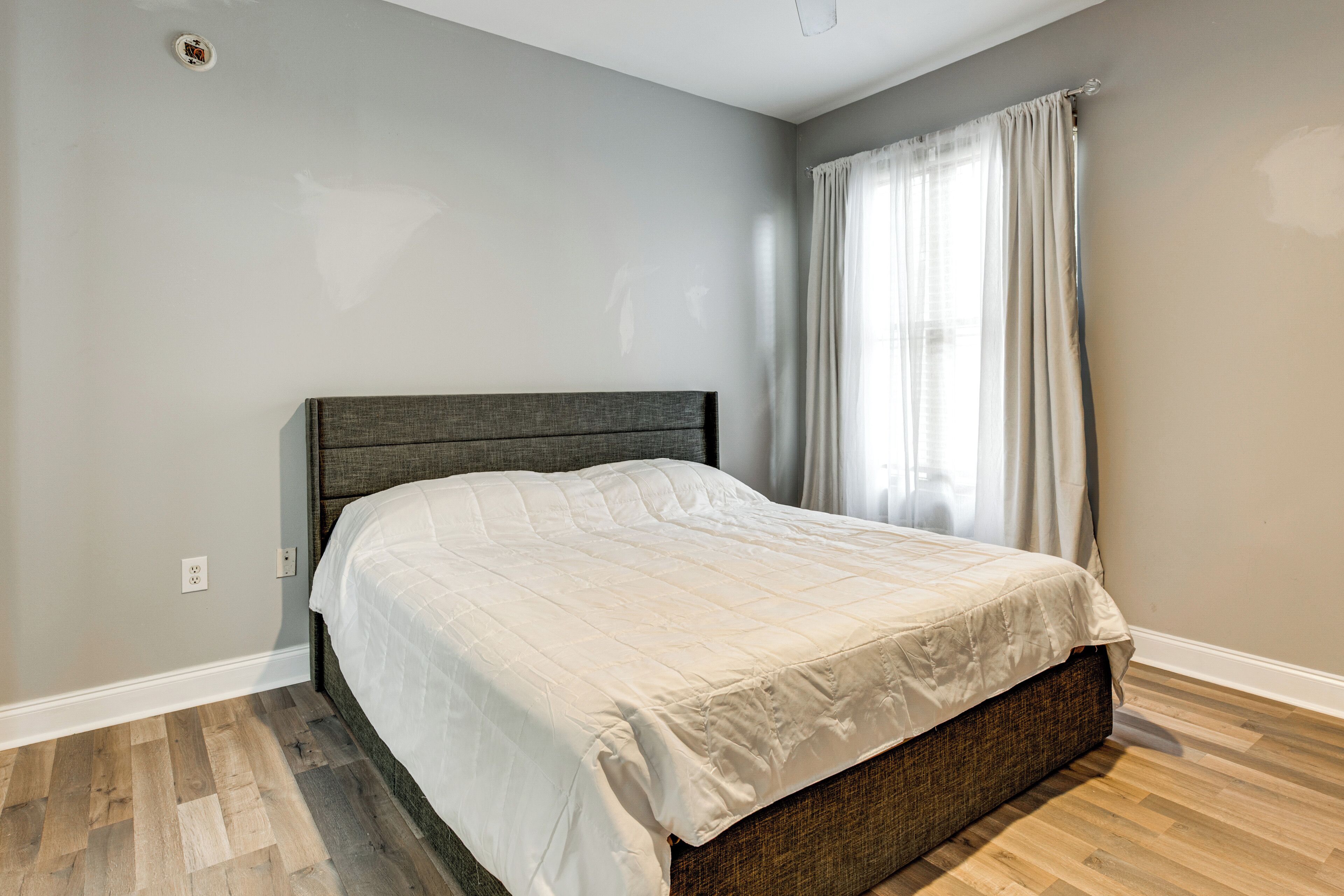 A bedroom with a bed, a window with curtains, and a light switch on the wall.