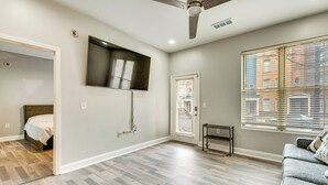 A spacious room with hardwood flooring, a ceiling fan, a mounted flat-screen TV, a door with blinds, and a sofa with a cushion. - Prime ATL Spot! Updated Condo Steps to Marta (Atlanta)