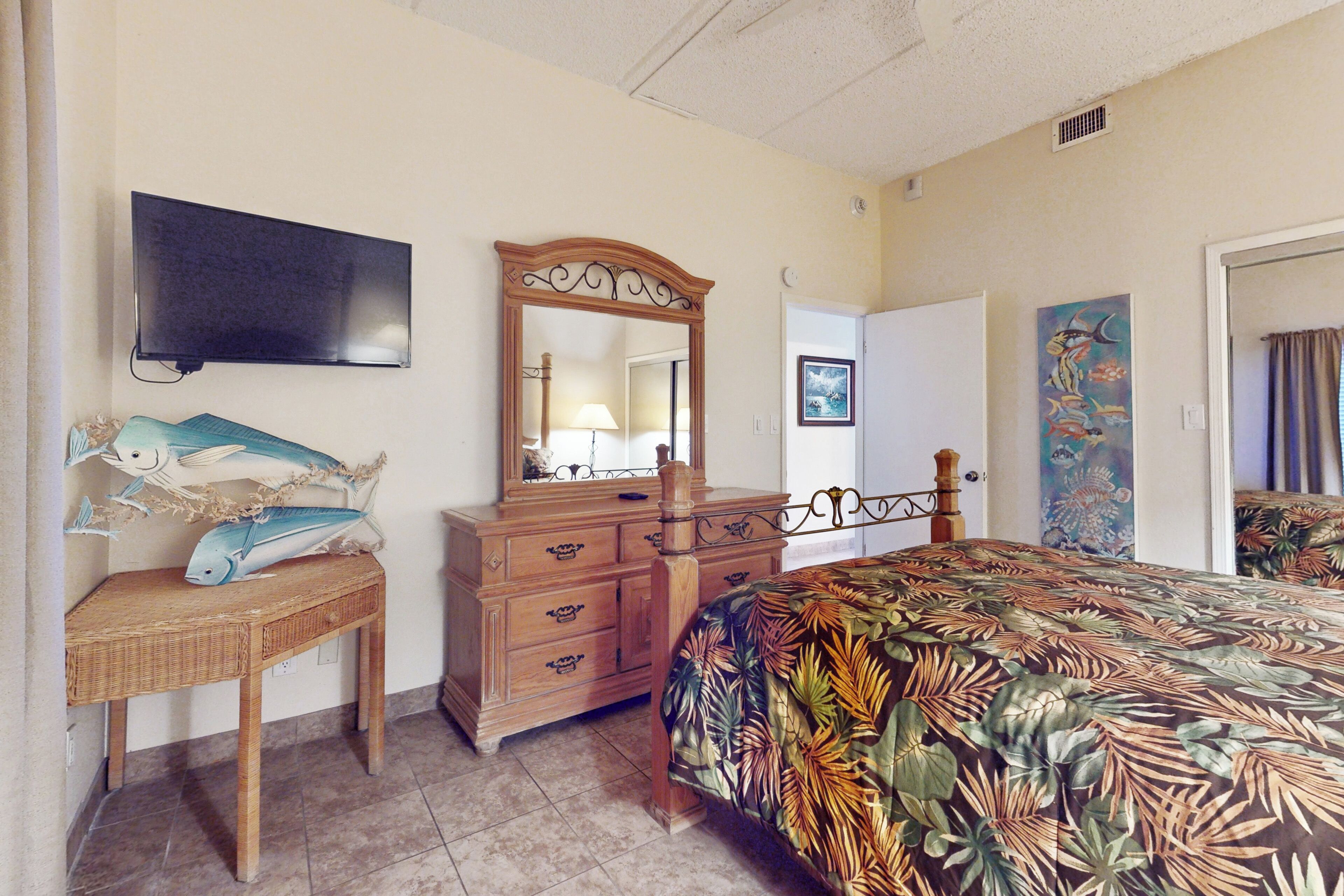 A bedroom with a bed, dresser, television, and artwork on the wall.