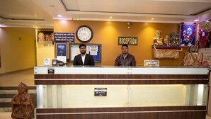 A reception desk with two staff members, a clock, and a reception sign. - Hotel Tulusi Inn (Digha)