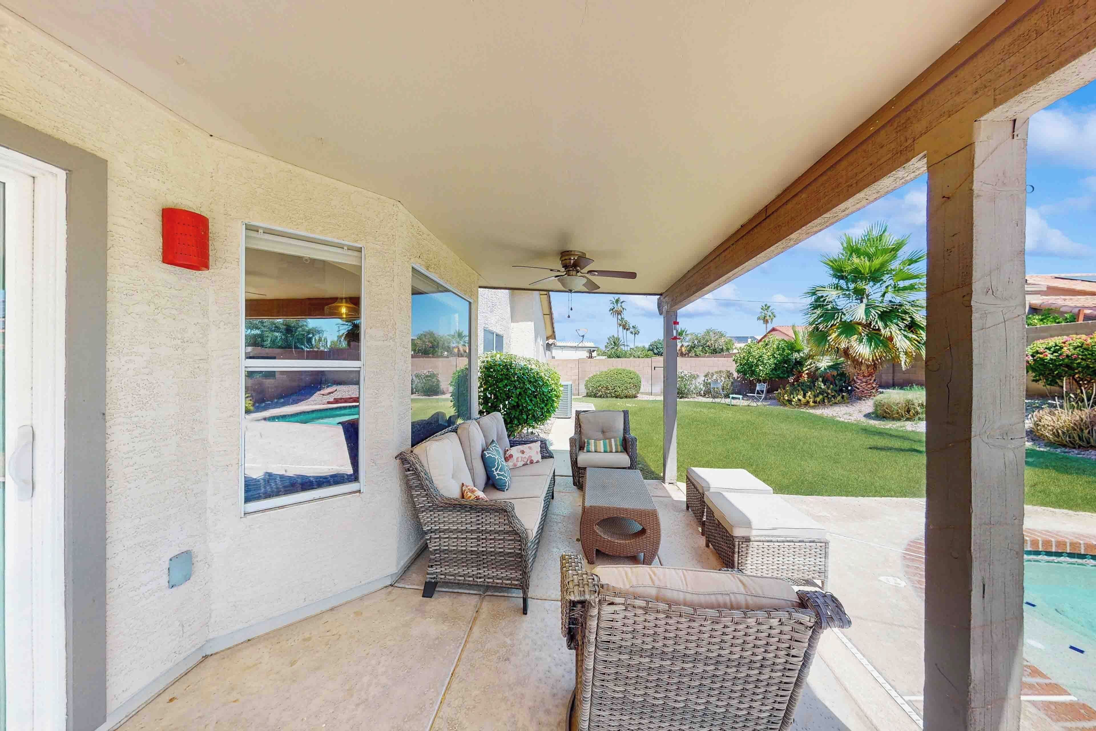 A covered patio area with wicker furniture, a ceiling fan, and a view of a swimming pool and garden.