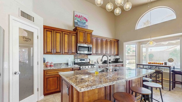 A kitchen with wooden cabinets, granite countertops, a large island with stools, and a view to the outside. - Private Pool, Yard & Pool Table! 'avondale Abode' (Avondale)