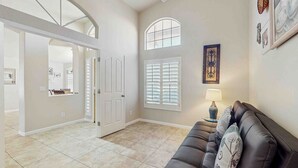 A spacious living area with a leather sofa, a dining table, and a large window with shutters. - Private Pool, Yard & Pool Table! 'avondale Abode' (Avondale)