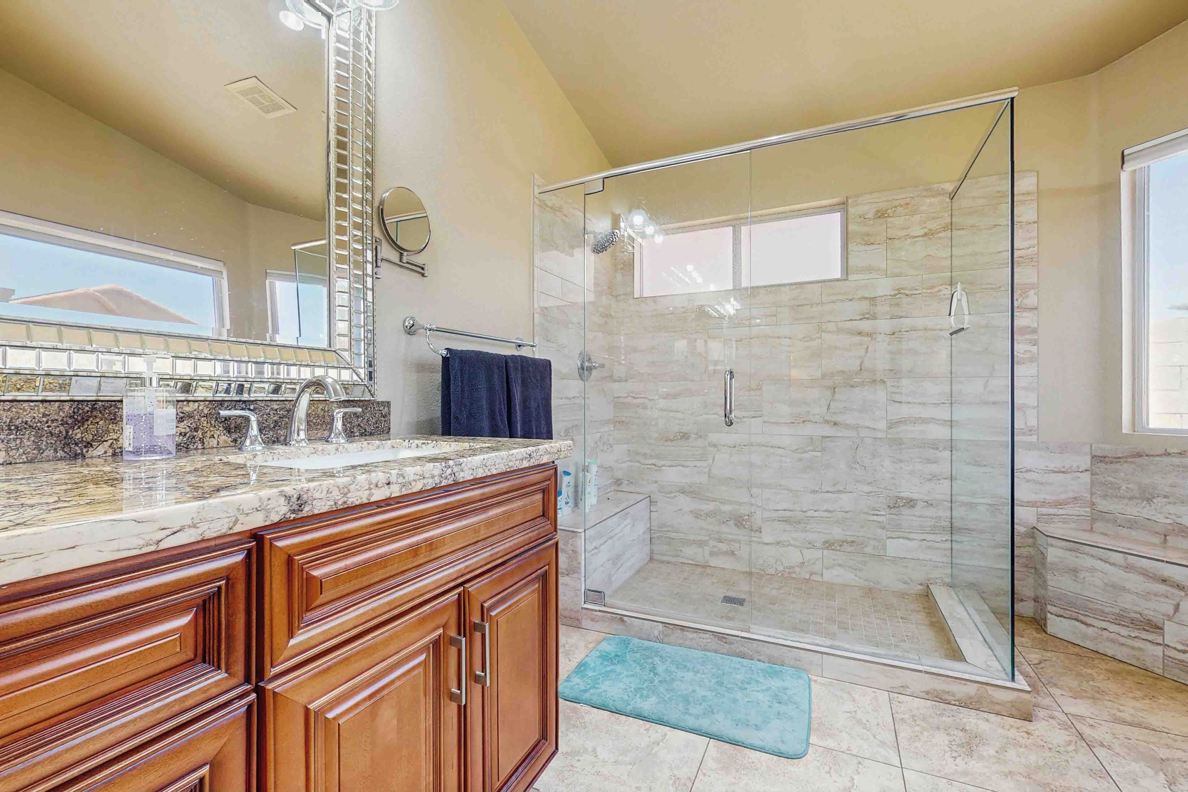 Un baño con cabina de ducha de vidrio, muebles de madera, encimera de mármol y un espejo grande.