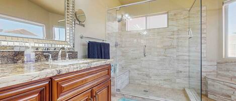 Un baño con cabina de ducha de vidrio, muebles de madera, encimera de mármol y un espejo grande.