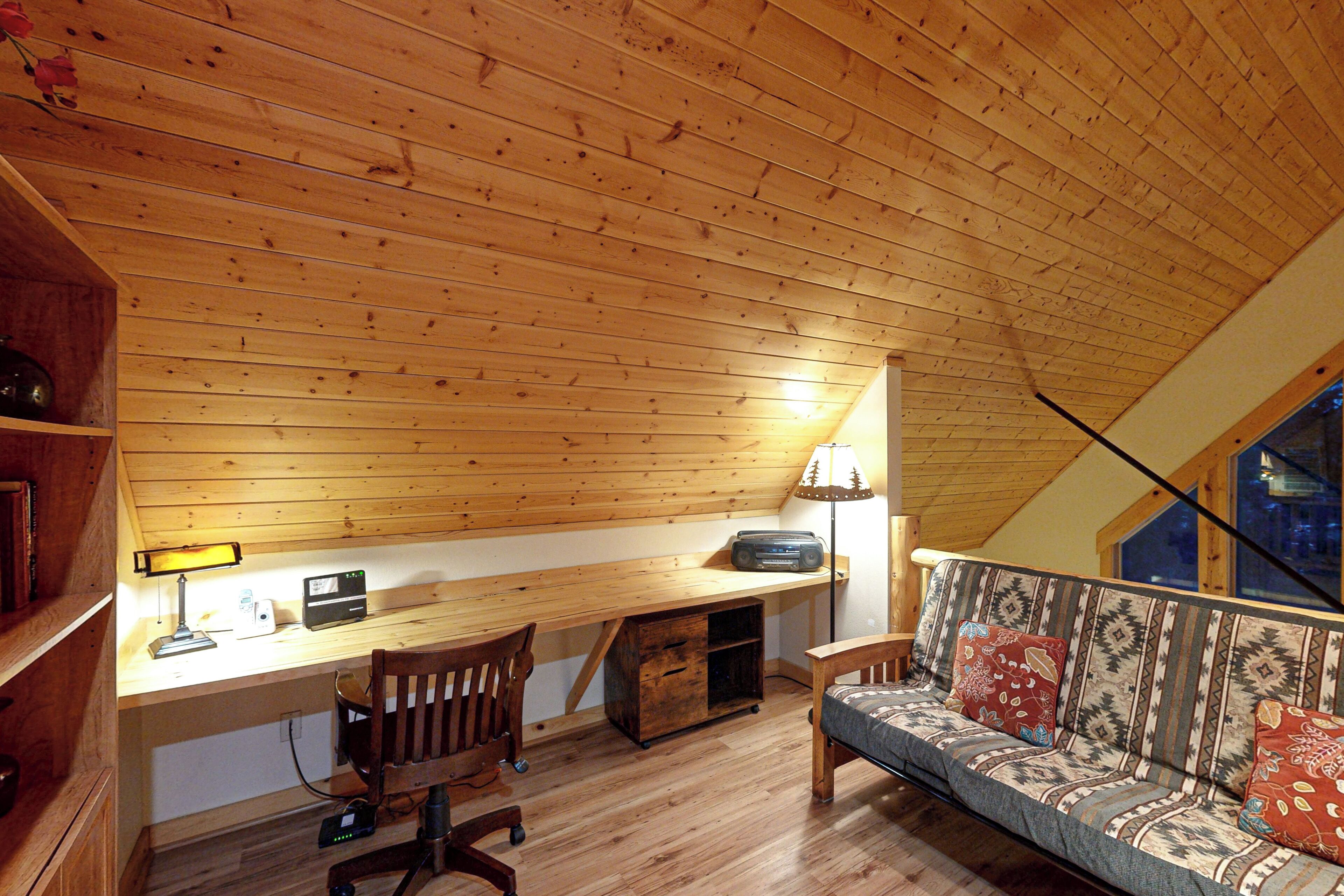 Ein gemütliches Dachzimmer mit einem Holztisch, Stuhl und einer Couch mit gemusterten Kissen.