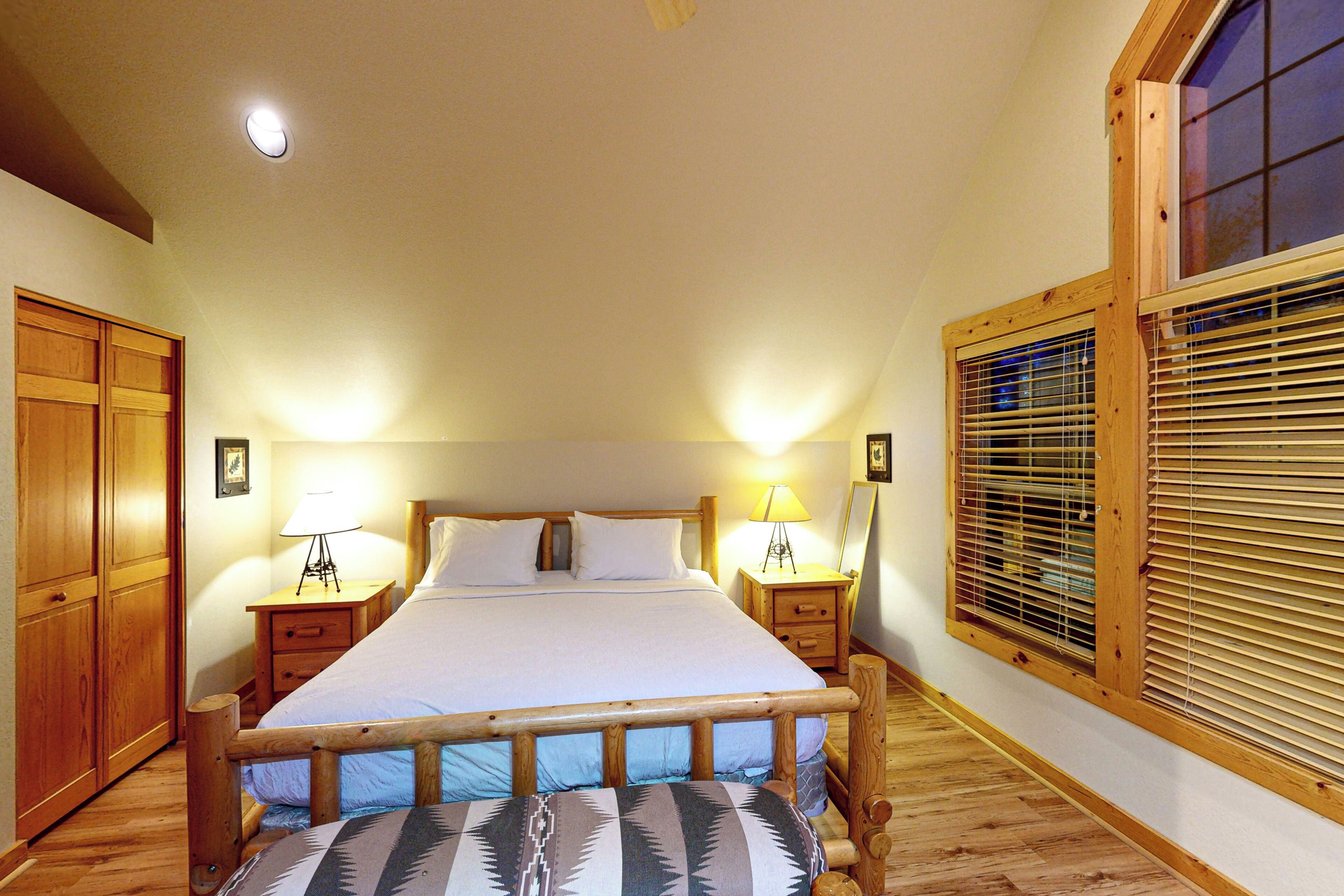 Un dormitorio con estructura de cama de madera, dos mesitas de noche con lámparas, un armario y una ventana con persianas.