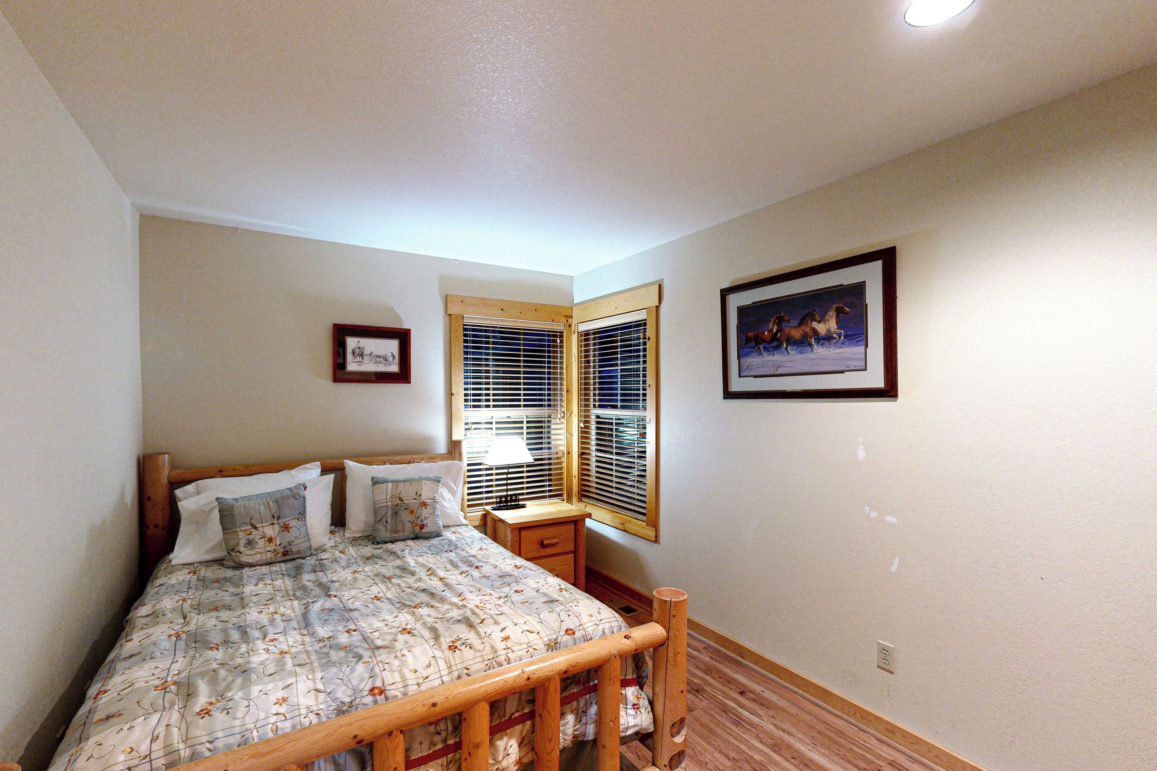 A bedroom with a bed, a nightstand, a window with blinds, and a framed picture on the wall.