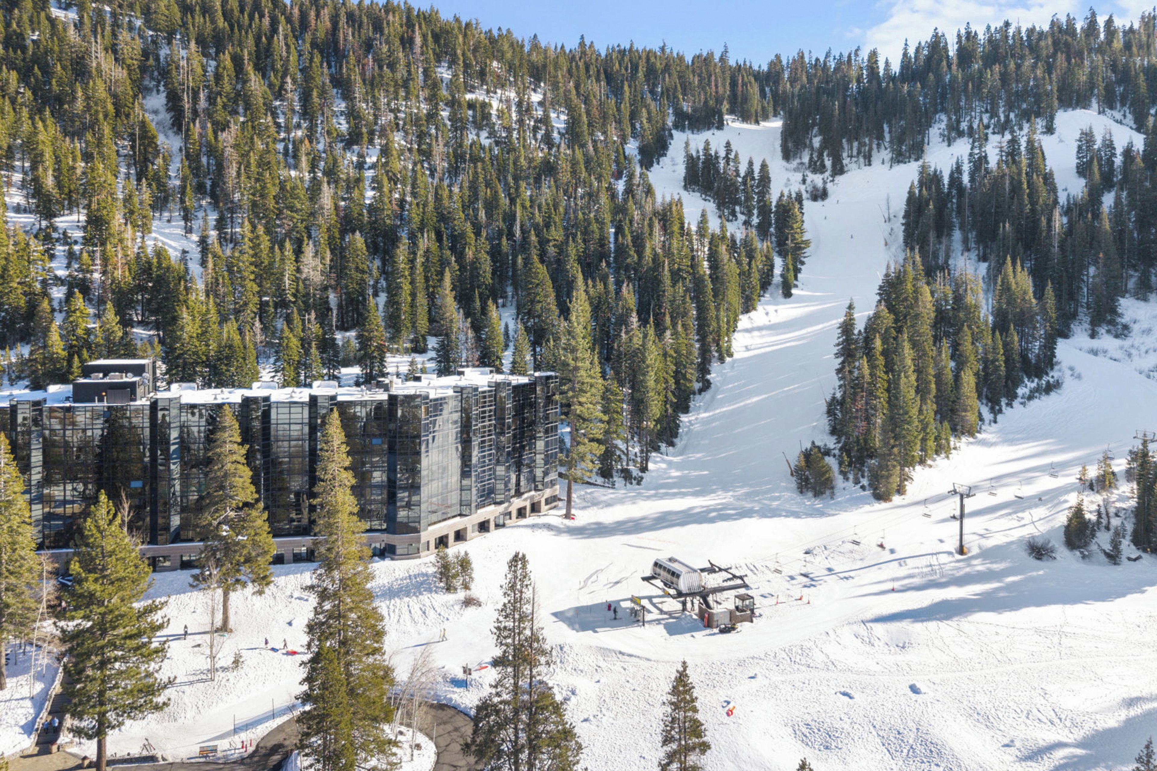 A modern ski resort building surrounded by snow-covered slopes and dense pine trees.