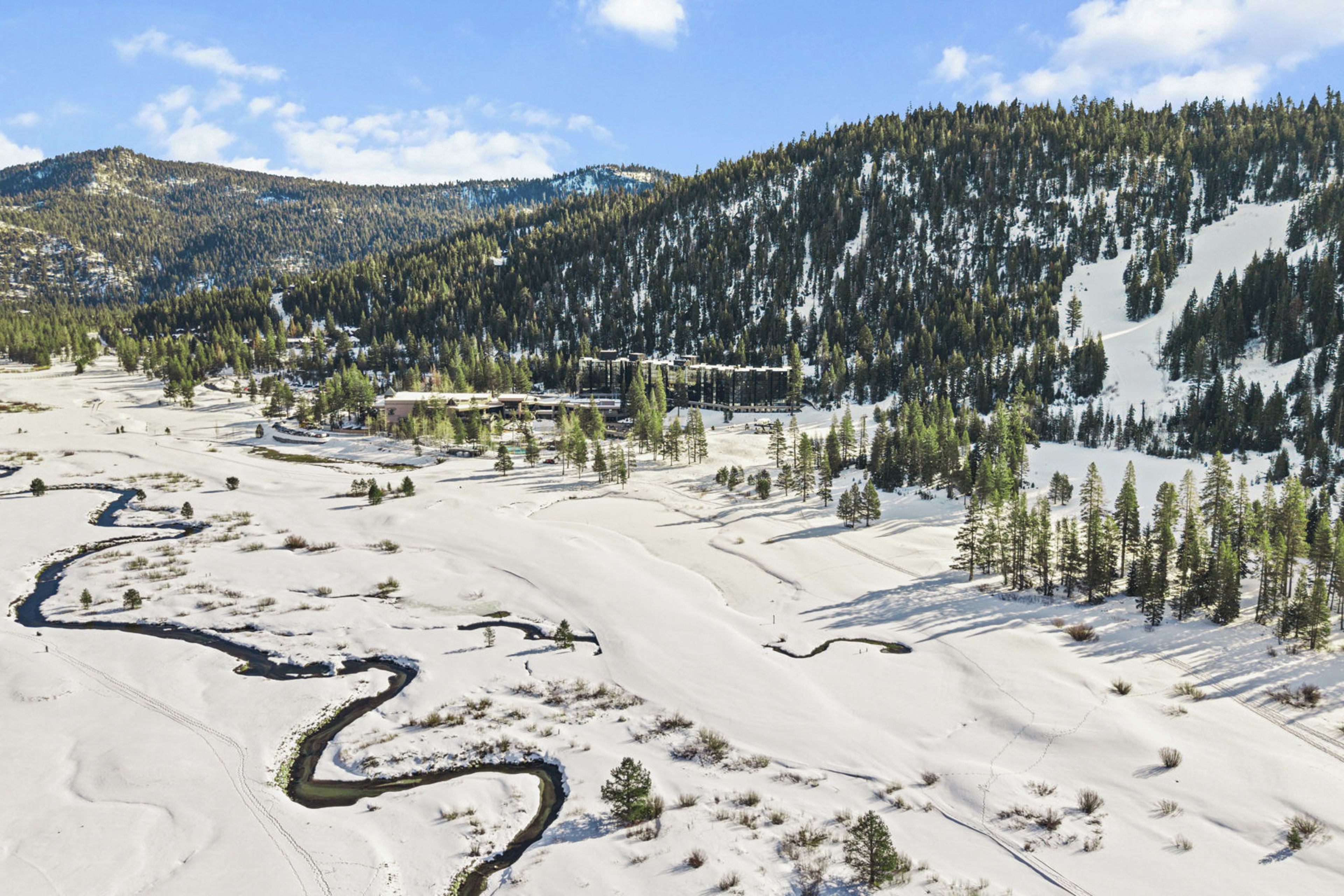 A snow-covered landscape with a river, trees, and a mountainous backdrop.