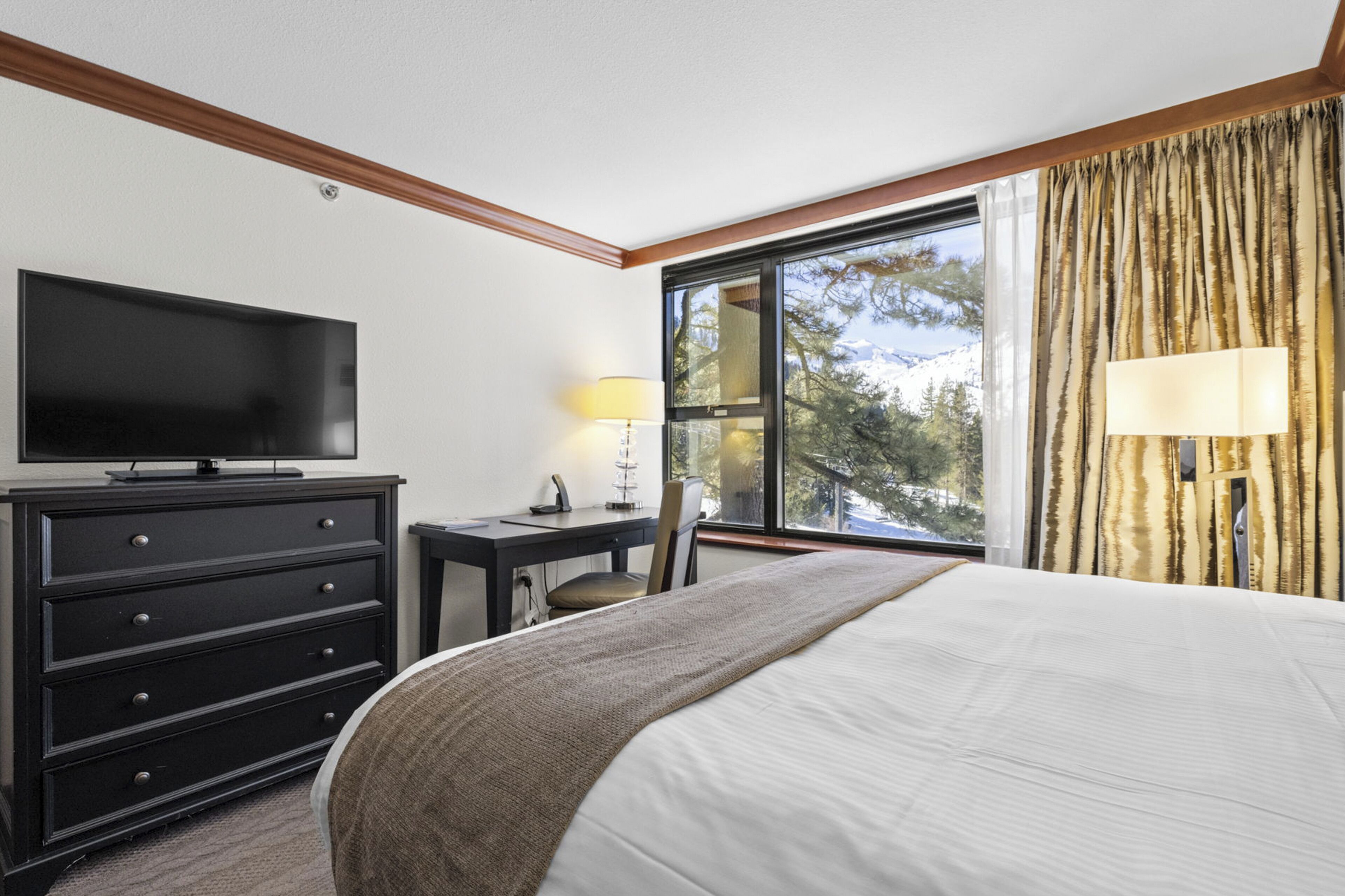Une chambre d’hôtel avec un lit, un bureau, une télévision et une fenêtre avec des rideaux.