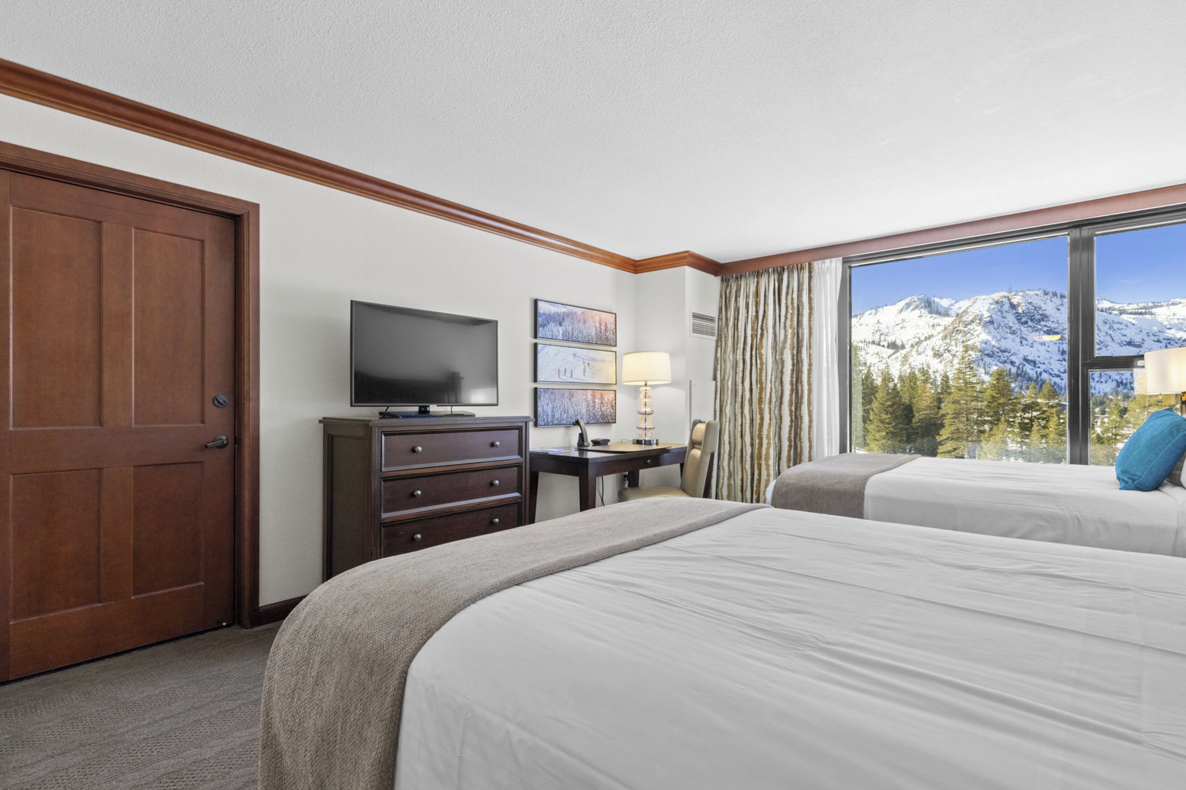 Una camera d'albergo con un letto grande, una scrivania, una televisione e vista sulle montagne innevate.