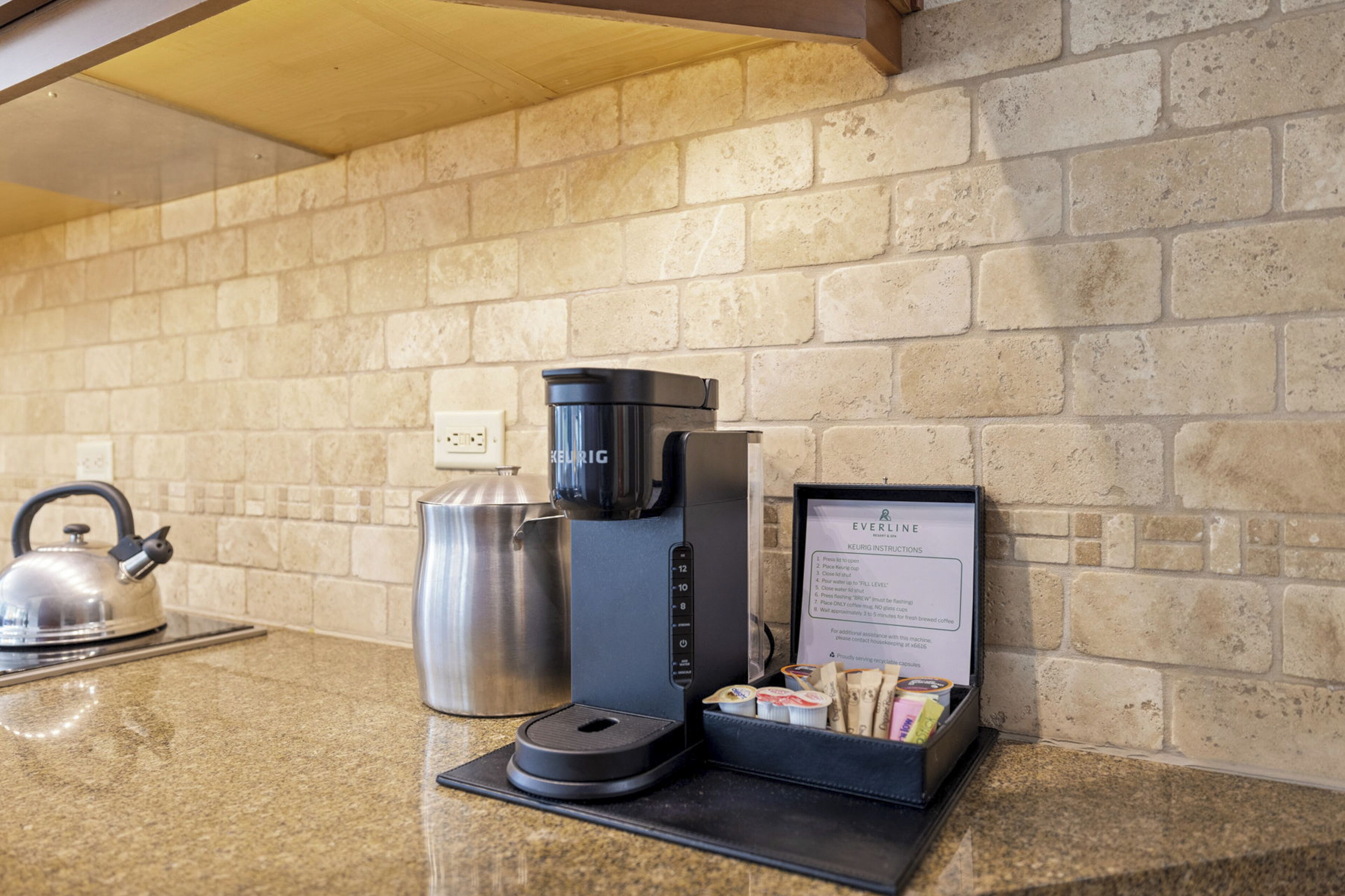 A coffee station with a coffee maker, a kettle, and a menu on a countertop.