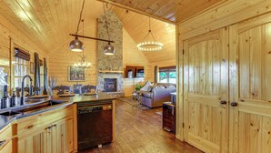 Eine geräumige Küche mit Holzausstattung, einem Geschirrspüler und einem Kamin aus Stein. Es gibt eine Essecke mit einem großen Holztisch und einer Couch.