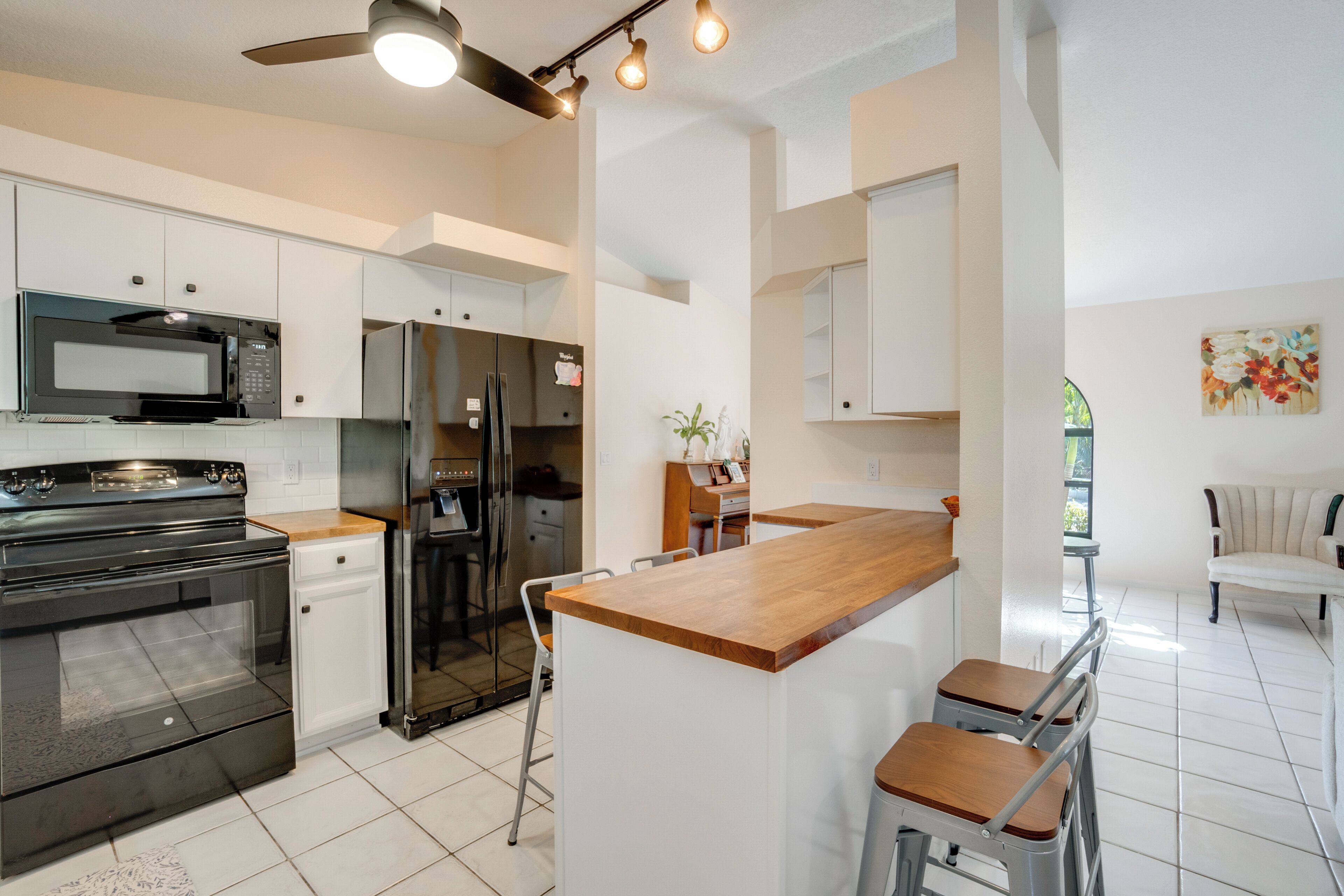 A modern kitchen with white cabinets, a wooden countertop, a built-in microwave, and a stainless steel refrigerator.