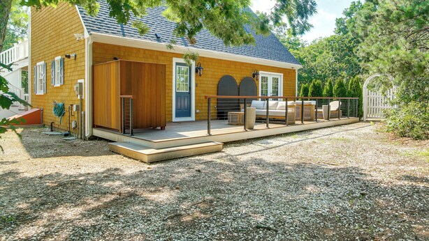 A wooden house with a covered porch, a fenced outdoor seating area, and a gravel driveway. - Summer Beach Pass: Wooded Martha's Vineyard Escape (Vineyard Haven)