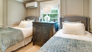 A bedroom with two beds, a dresser, and an air conditioning unit. - Summer Beach Pass: Wooded Martha's Vineyard Escape (Vineyard Haven)