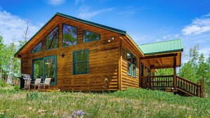 A wooden cabin with large windows, a deck, and a grassy surrounding.