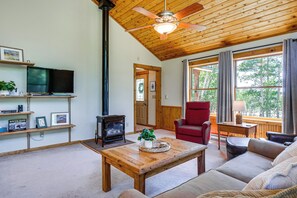 A cozy living room with a wooden ceiling, a television, a fireplace, a red armchair, and a large window with a view of trees. - Fairplay Cabin Mountain Views, Trails, Fishing (Fairplay)