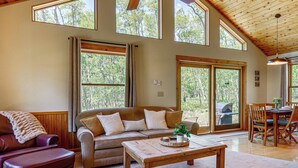 A spacious living room with a large window, a wooden ceiling, a sofa, a coffee table, and a dining area.
