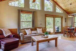 A spacious living room with a large window, a wooden ceiling, a sofa, a coffee table, and a dining area. - Fairplay Cabin Mountain Views, Trails, Fishing (Fairplay)