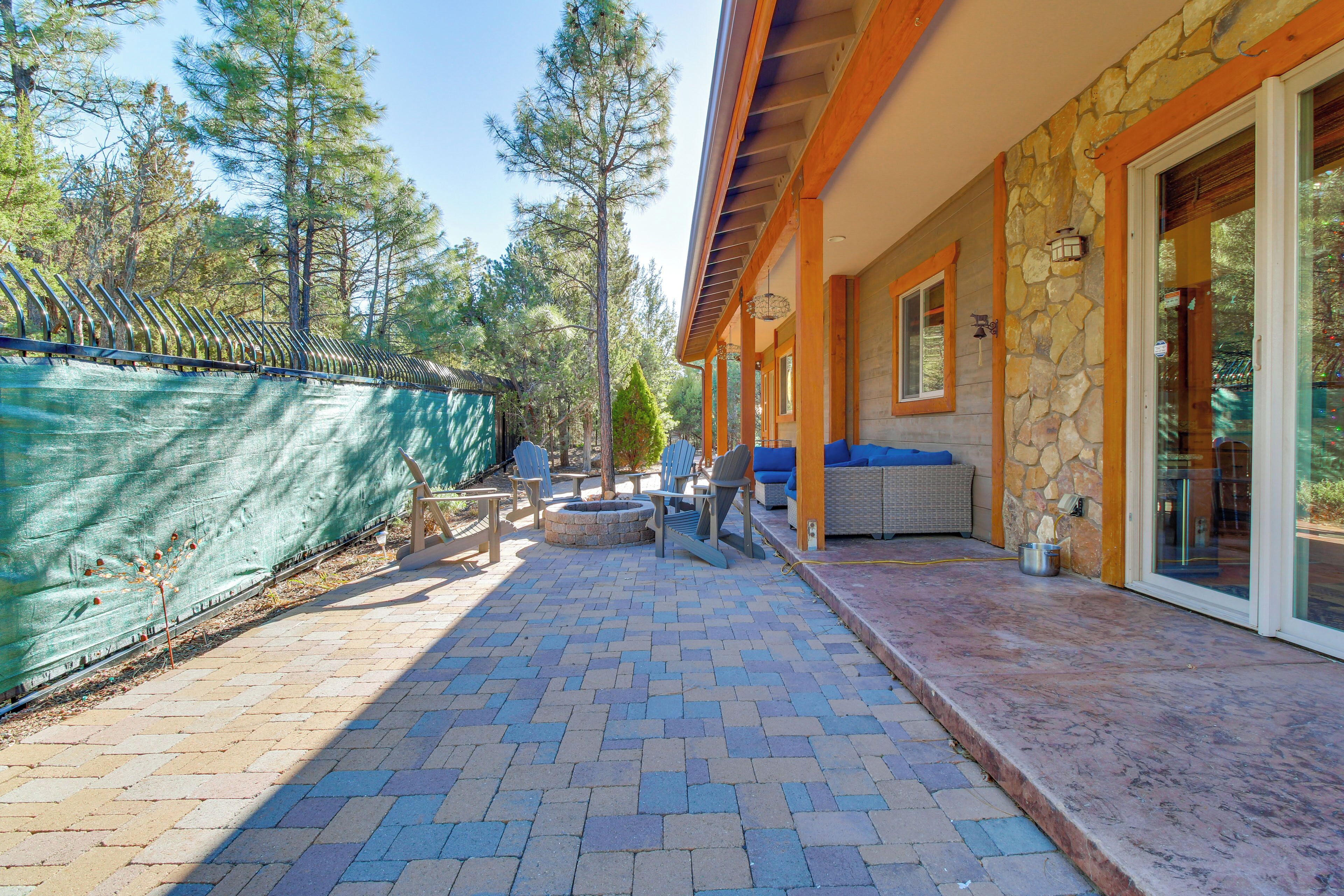 A covered patio with a stone wall, outdoor seating, and a view of a forested area.