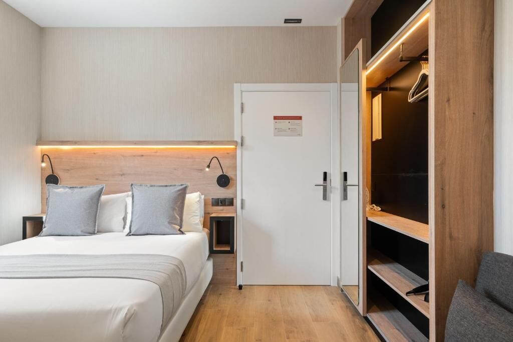 A modern hotel room with a bed, bedside tables, a wardrobe, and a door with a sign.