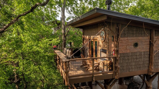 Ein Baumhaus mit einer Holzterrasse, Kamin und einer Uhr.